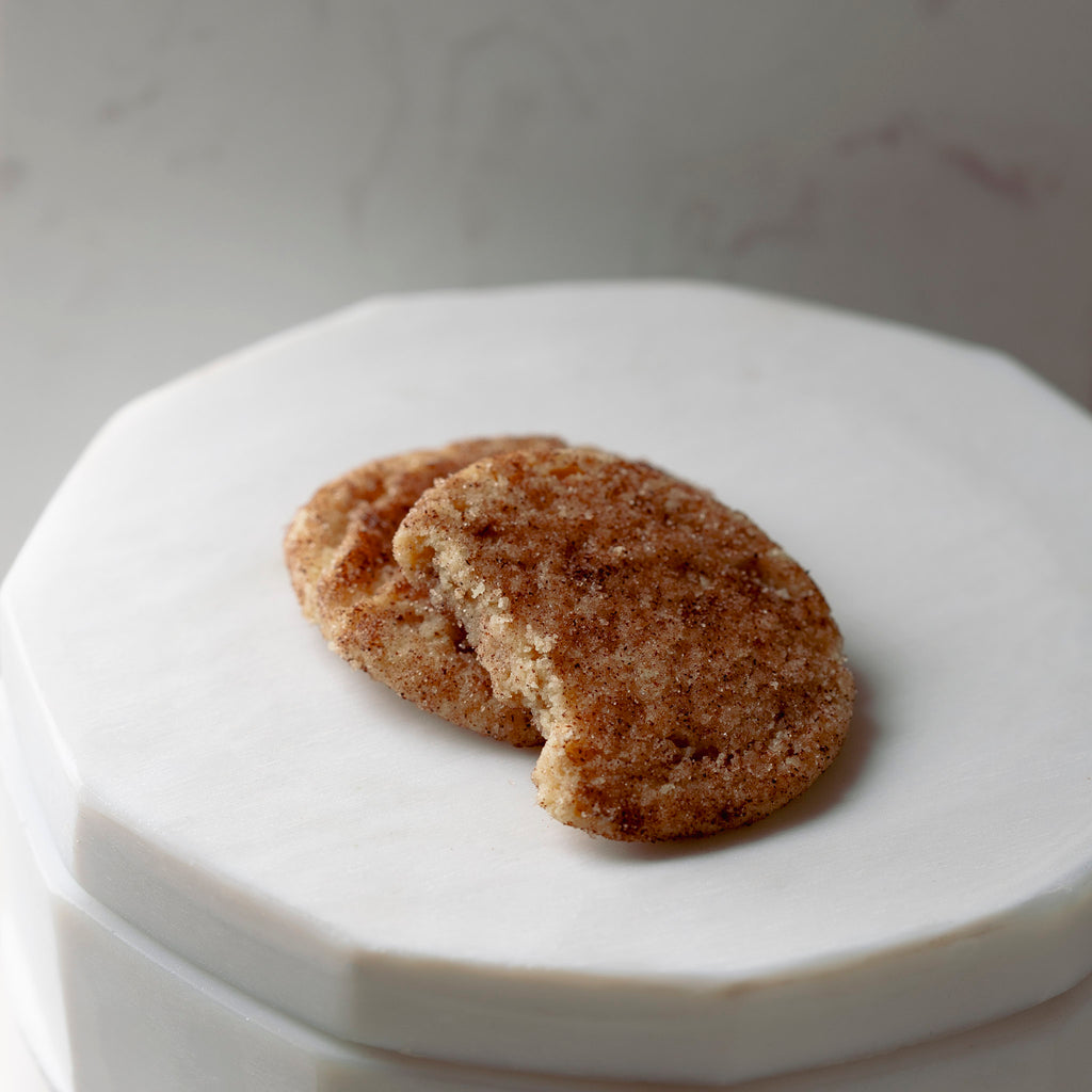 Two Snickerdoodle cookies are sitting on a marble container.  One of the cookies has a bite out of it.