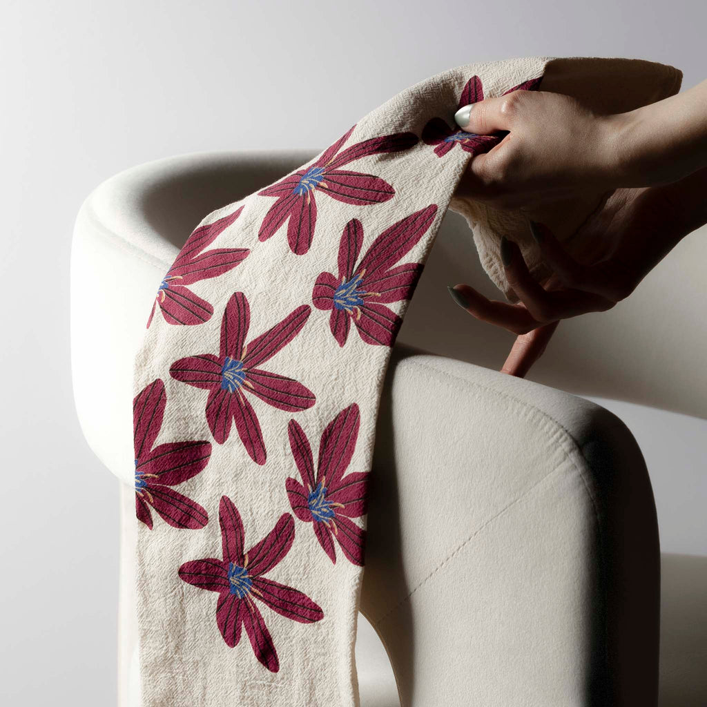 A Tea Towel in Pink Rain Lilly Flower from Line + Nest is draped over an arm of a chair and is being picked up.