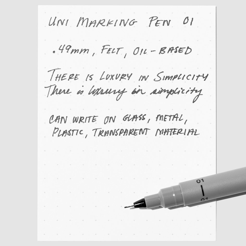 Uni Pin Marking Pen, 01, Cloth and Paper. Pen resting on paper displaying writing sample.