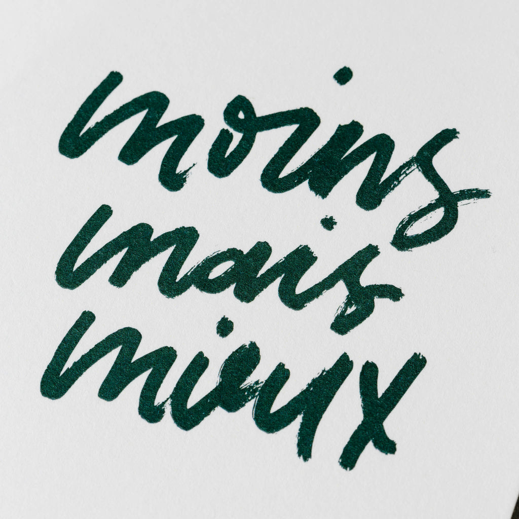 Closeup of dark green printed text that reads "moins mais mieux" in script handwriting.