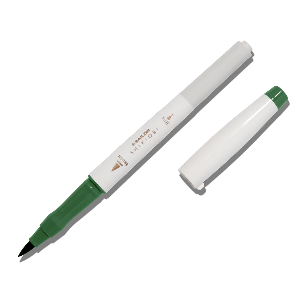 Brush pen displayed on a white background. It is uncapped with its brush nib exposed, and the cap lying parallel to the marker. Color pictured is Tokiwamatsu. 