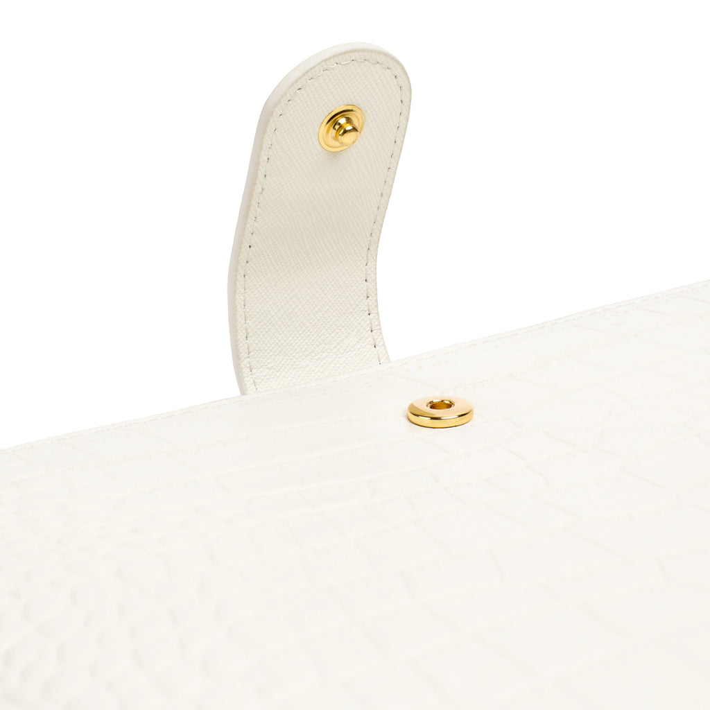 Closeup of gold clasp hardware on a white croc leather agenda cover.