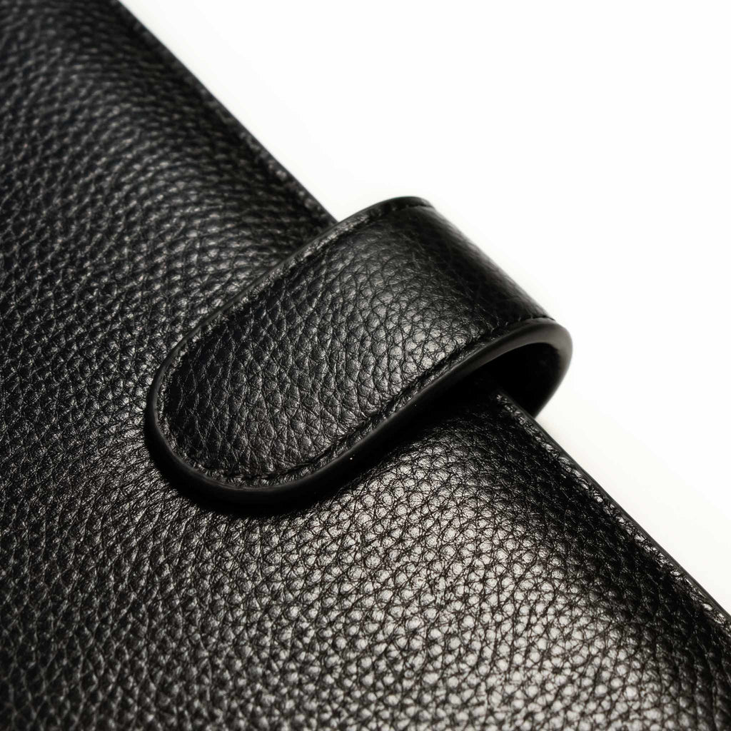 Close up on the closed snap detail and texture of a black smooth leather agenda cover.