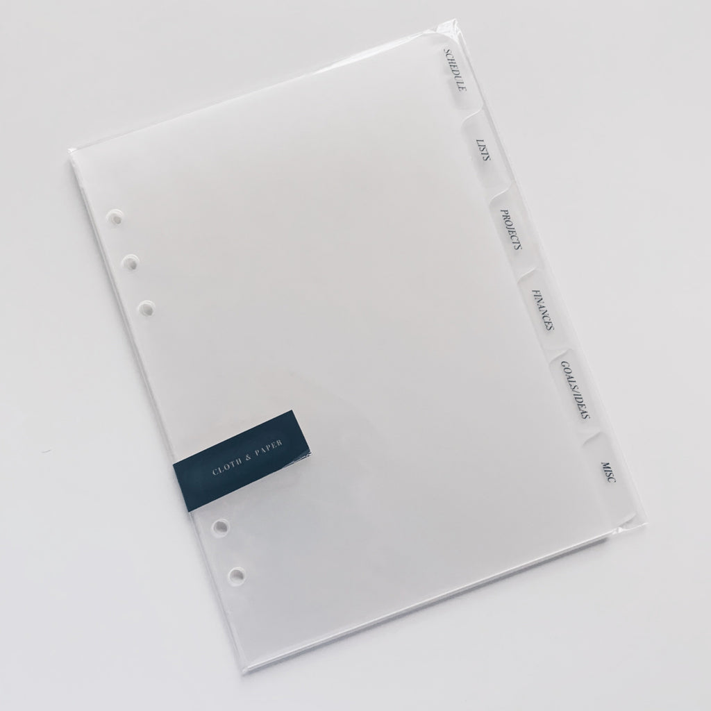 CEO Side Tab Planner Dividers, Glass Plastic, Black Foil, Cloth and Paper. Dividers in their packaging tilted to the left on a white background.