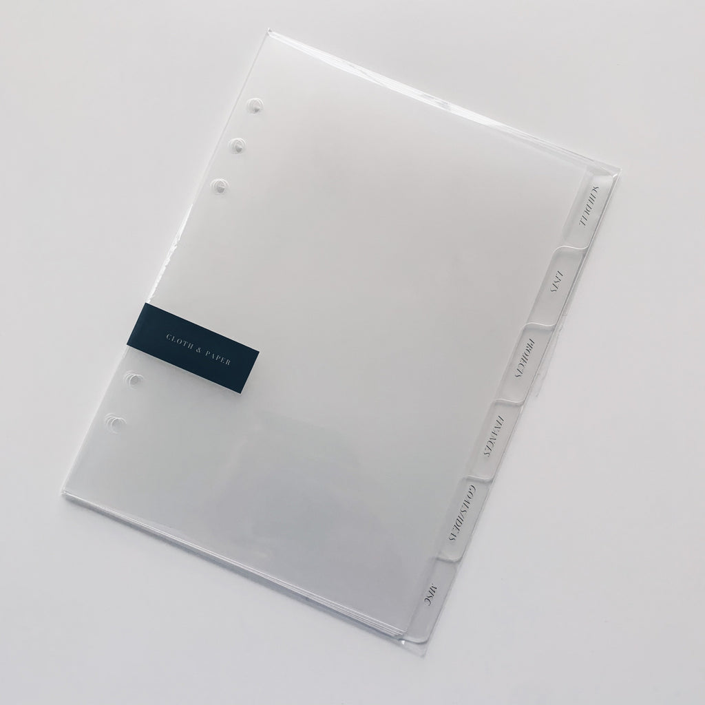 CEO Side Tab Planner Dividers, Glass Plastic, Gold Foil, Cloth and Paper. Dividers in their packaging tilted to the right on a white background.