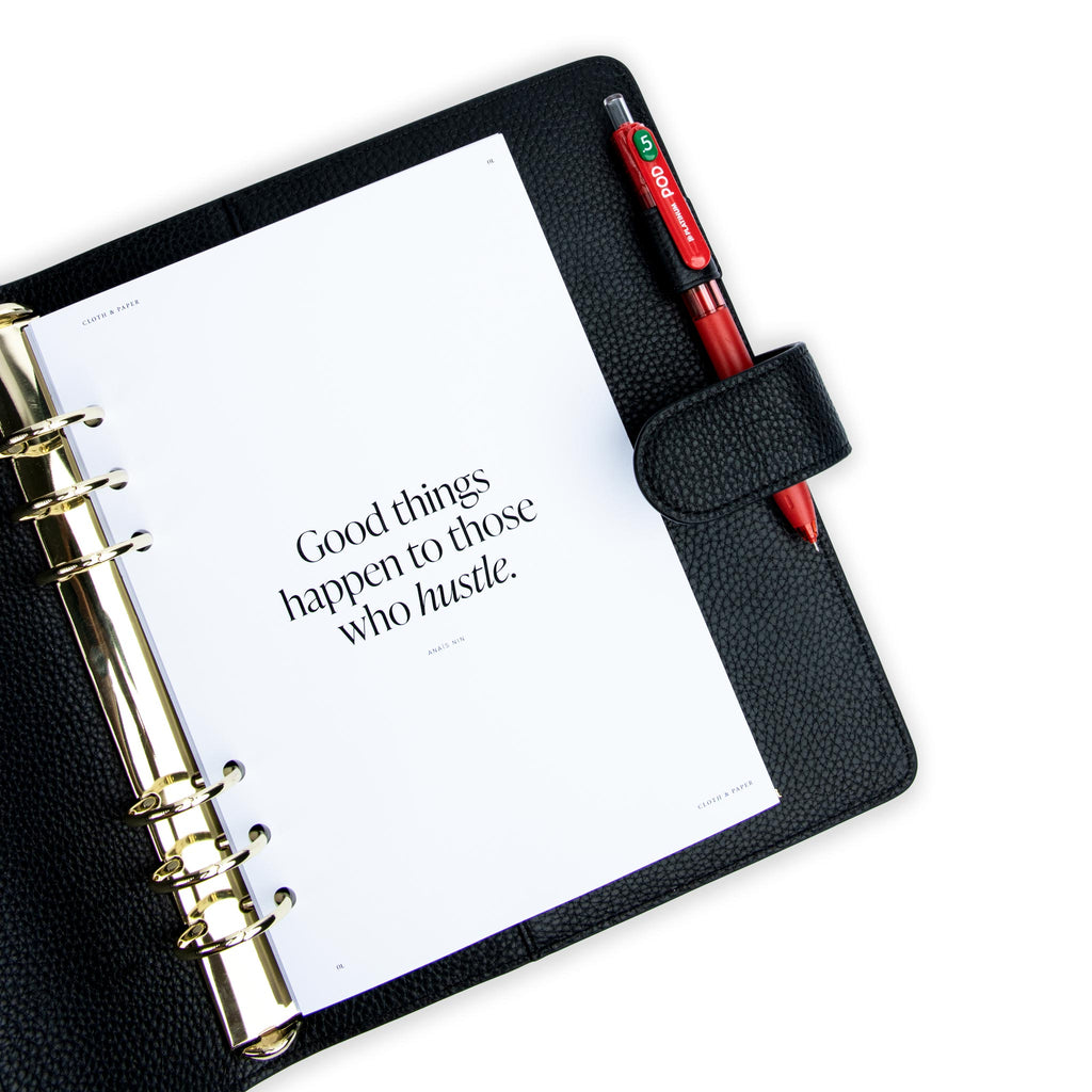 Creative Planning Insert Bundle, Cloth and Paper. Insert in use inside of a black leather agenda with gold rings on a white background. A red pen rests in the agenda's pen loop.