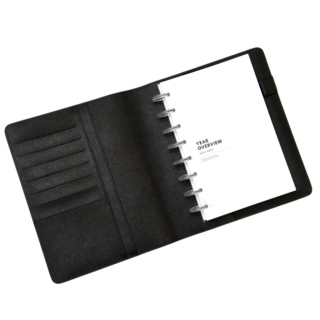 Black agenda folio opened to show a half letter discbound notebook inside of it. The discbound notebook has clear discs and some year overview inserts in it.