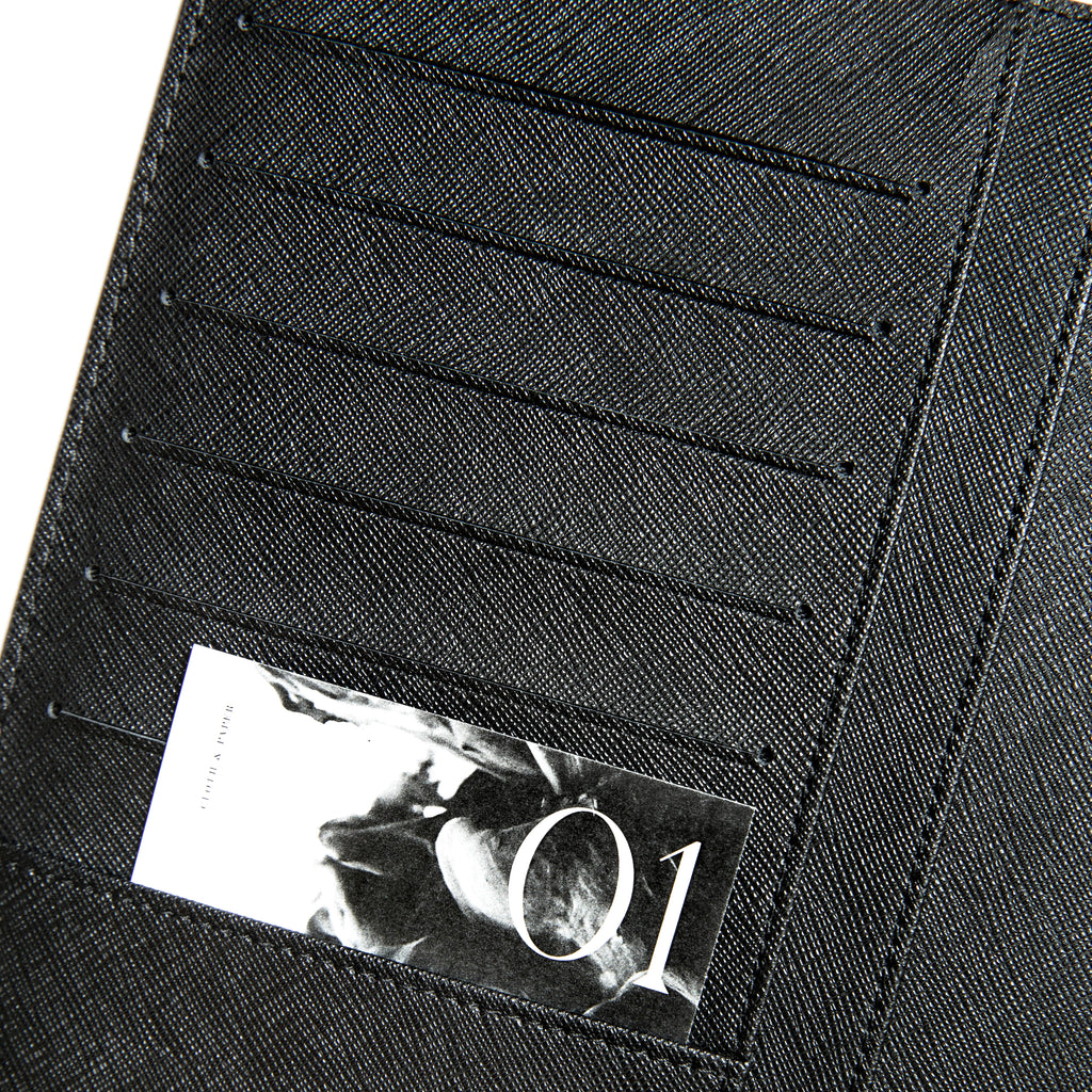 Close up on the credit card slots on the inside of the front cover of a black agenda folio. A black and white journaling card is tucked into the passport pocket underneath the credit card slots.