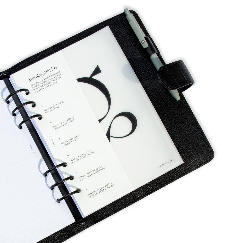 Daily Mindset Half Page Planner Dashboard styled inside a black leather 6-ring agenda. The agenda has a green pen tucked into its pen loop.