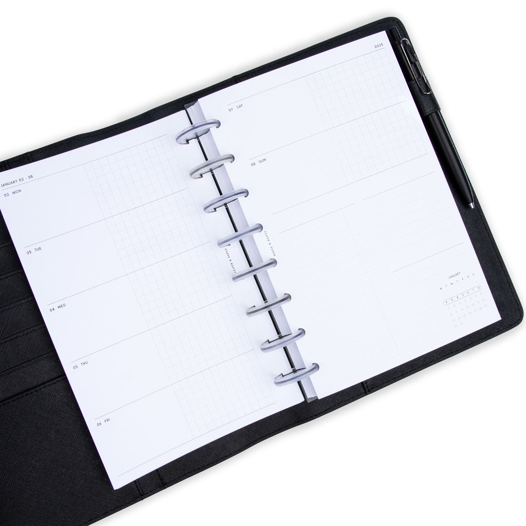 2023 Dated Planner Inserts, Horizontal Weekly, Cloth and Paper. Inserts in use inside of a black leather agenda with transparent rings on a white background. A black pen rests in the agenda's pen loop holder.