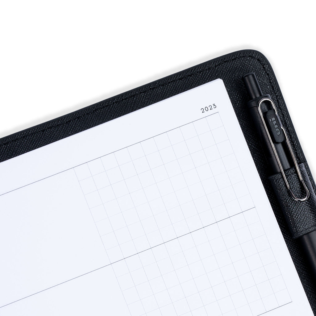 2023 Dated Planner Inserts, Horizontal Weekly, Cloth and Paper. Close up image of inserts in a black leather agenda holder. A black pen is resting inside of the agenda's pen loop.