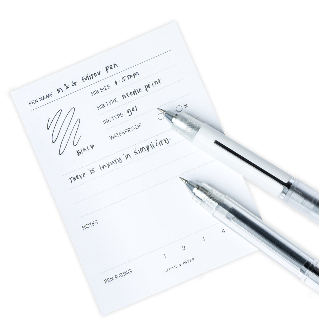 Clear and white pens resting on a pen test sheet displaying a writing sample that details the specs of the pens.