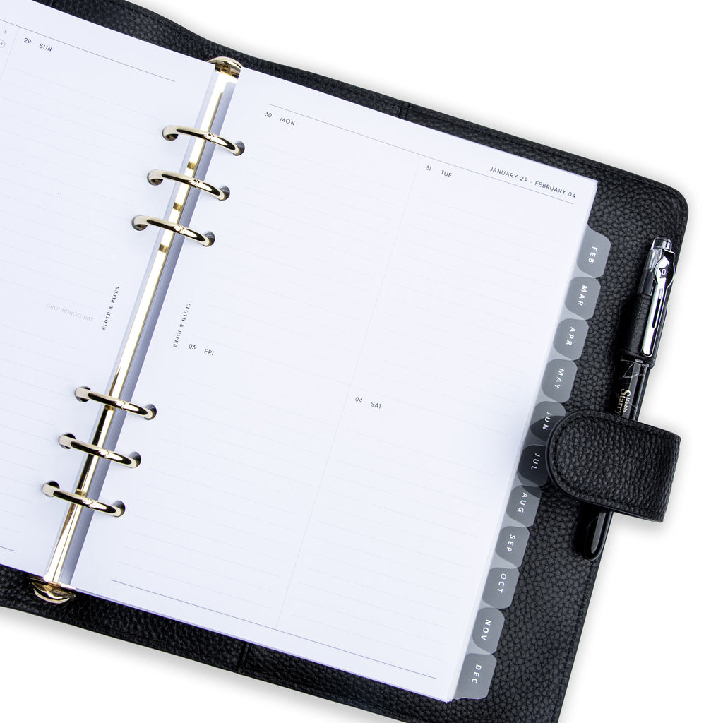 2023 Dated Planner Inserts, Vertical Weekly Lined, Sunday Start, Cloth and Paper. Inserts in use inside a black leather agenda with silver rings and clear monthly divider tabs. A pen rests in the agenda's pen loop.