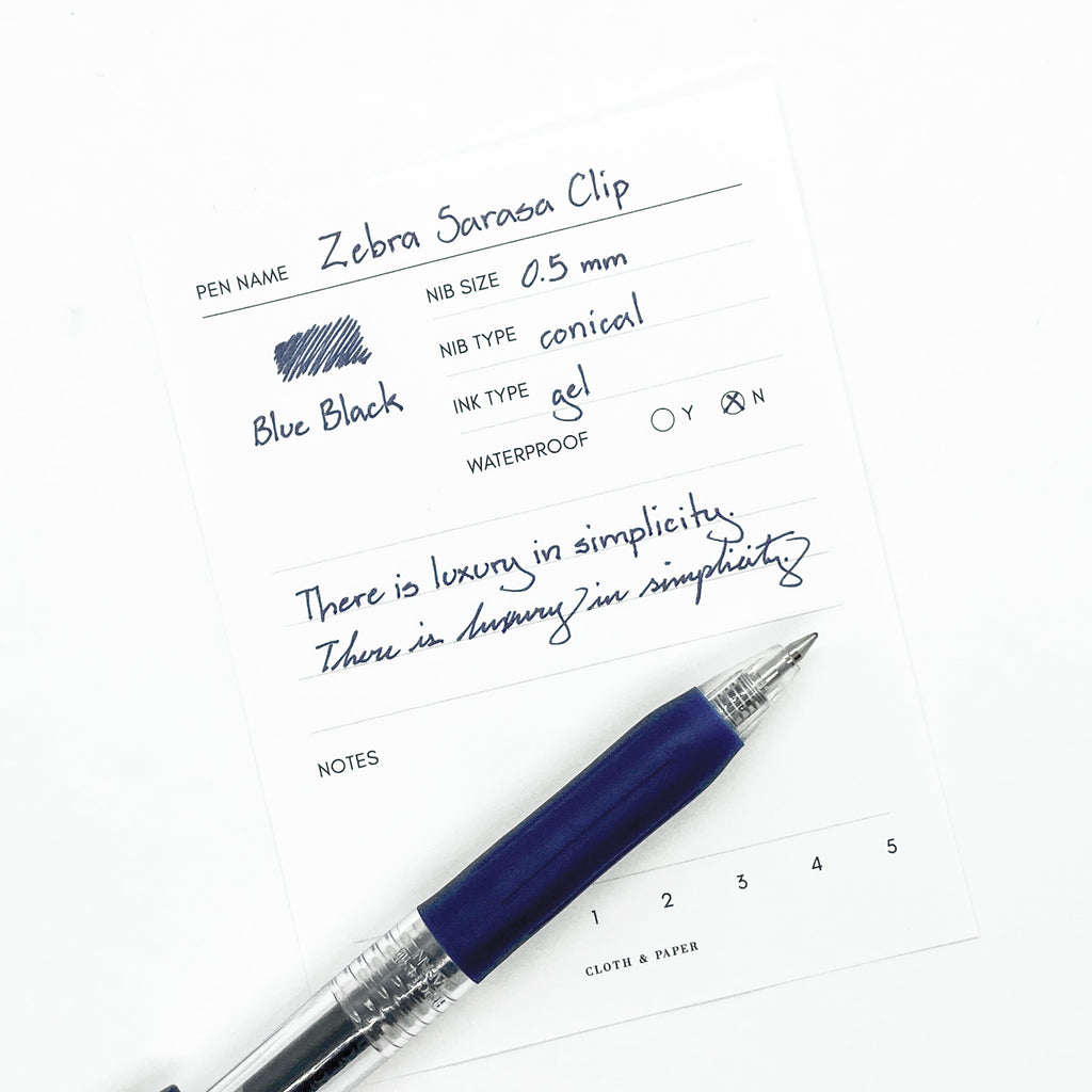 Zebra Sarasa Clip, 0.5 mm, Blue Black, Cloth and Paper. Pen resting on pen test sheet displaying writing sample.
