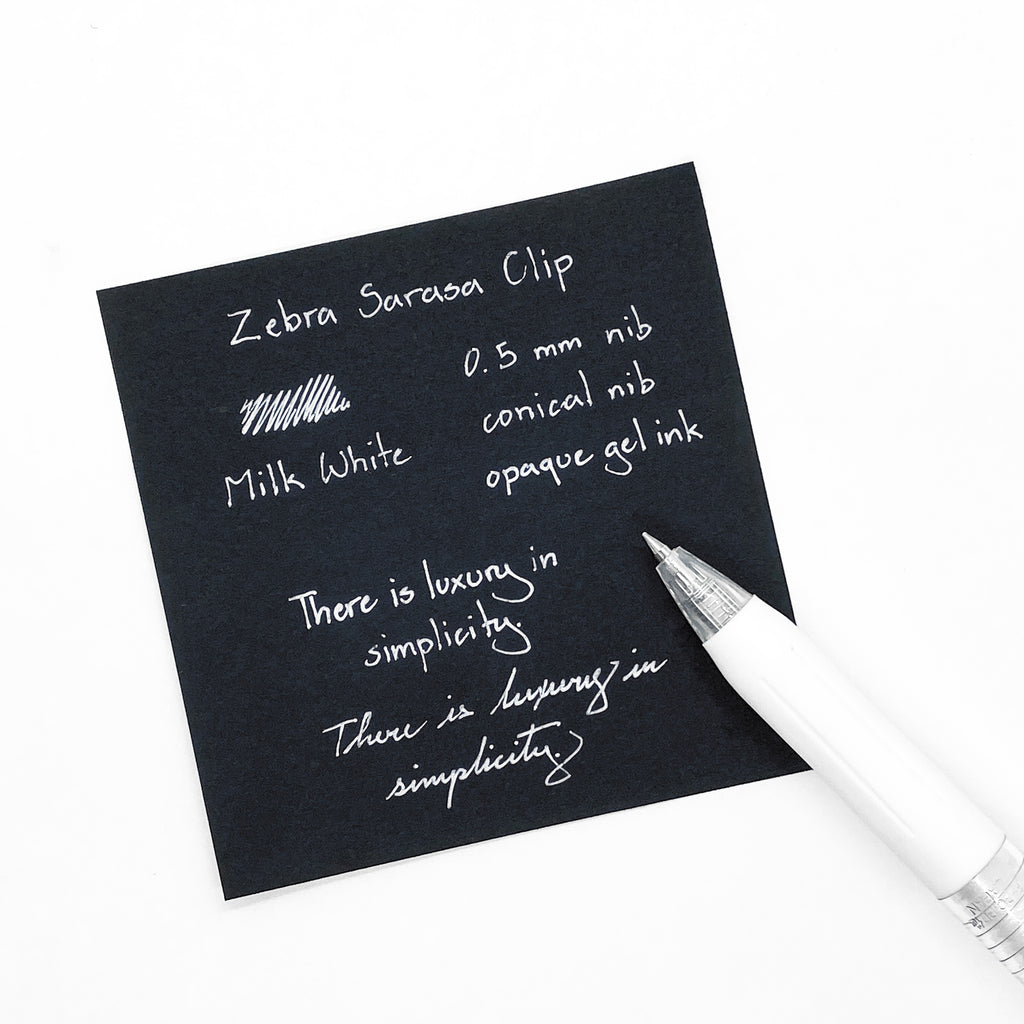 Zebra Sarasa Clip, 0.5 mm, Milk White, Cloth and Paper. Pen resting on black paper displaying writing sample.