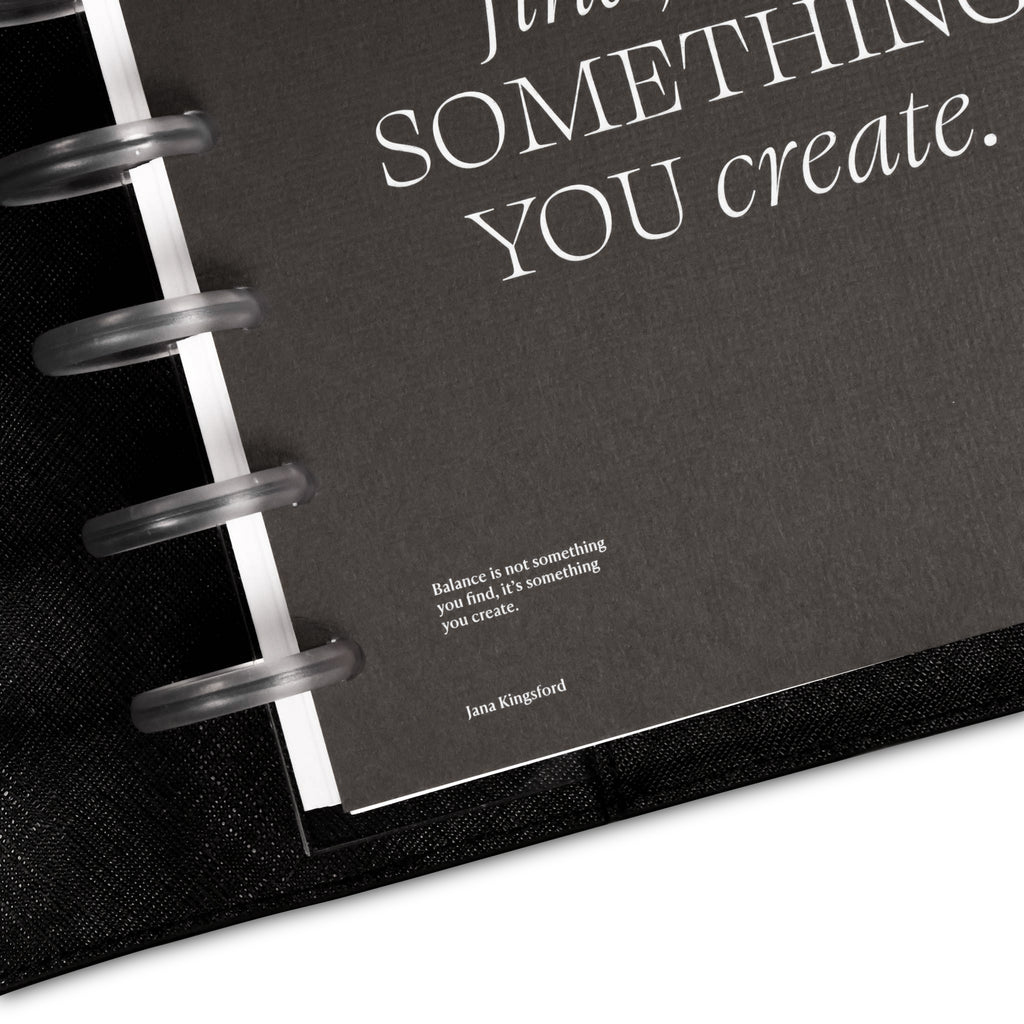 Close up on bottom left corner of dashboard styled inside a discbound planner and black leather cover. Text on dashboard reads "Balance is not something you find, it's something you create. Jana Kingsford"