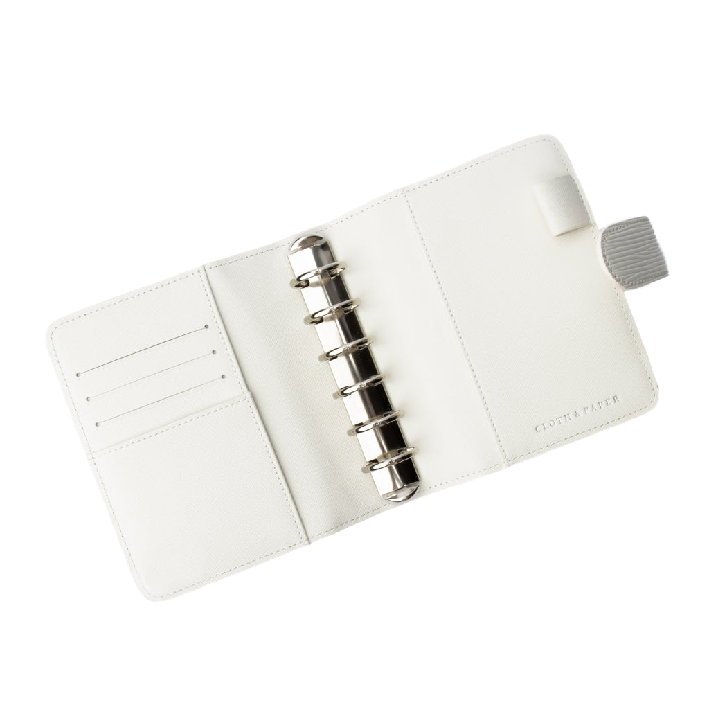 White agenda opened to show silver rings inside. The credit card slots and document pockets on the inside of the front and back covers are visible. The planner is empty.