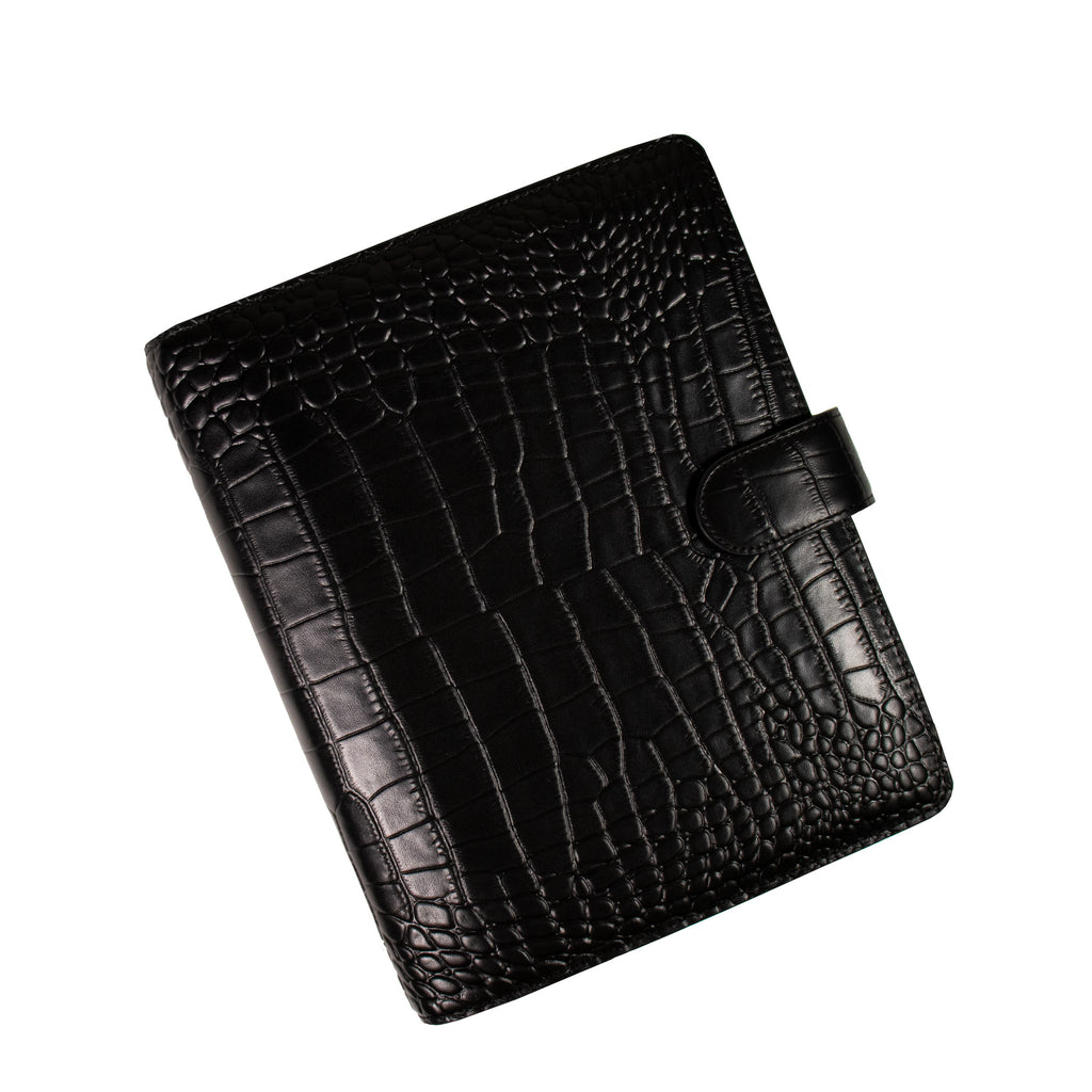 Black croc leather agenda cover closed to show the front cover, turned to the left against a white background.