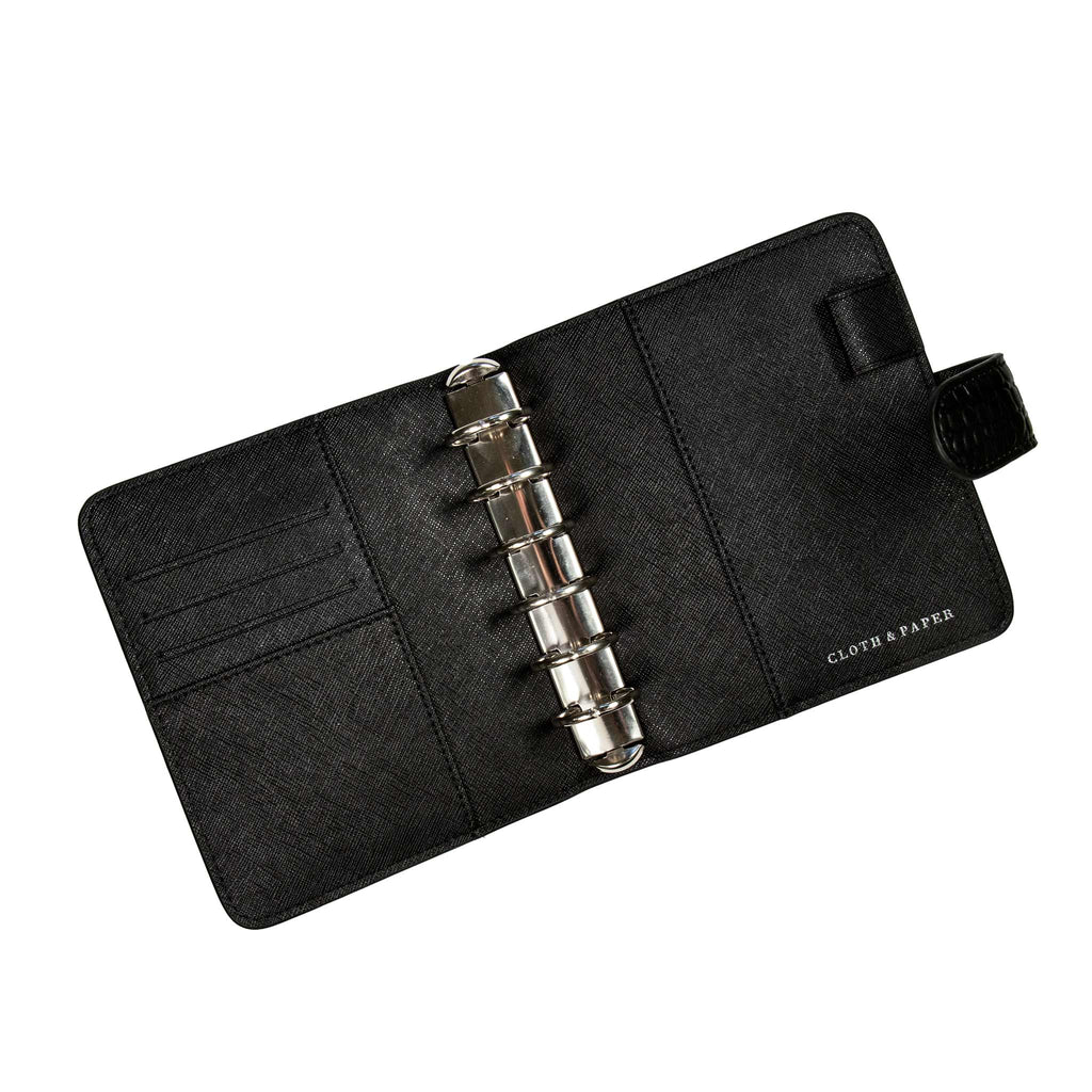 Black agenda opened to show silver rings inside. The credit card slots and document pockets on the inside of the front and back covers are visible. The planner is empty.