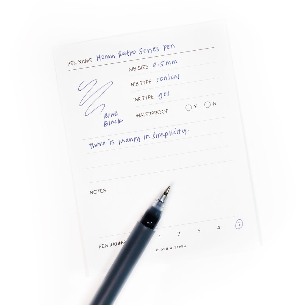 Pen in Blue resting on a pen test sheet displaying a writing sample of the pen's specs.
