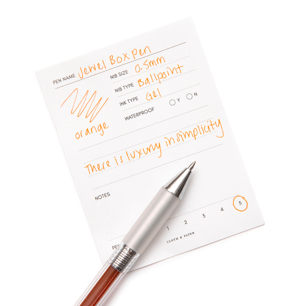 Jewel Box Pen, Orange, Cloth and Paper. Pen resting on a pen test sheet displaying a writing sample against a white background.