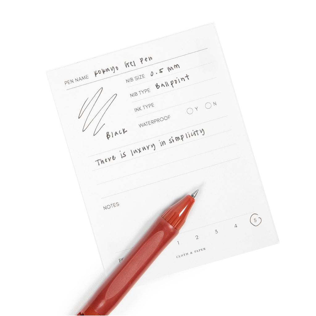 Red pen resting on a pen test sheet displaying a writing sample detailing the pen's specs.