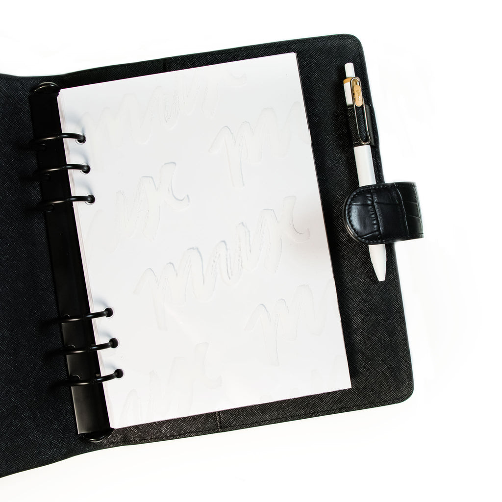 Dashboard styled inside a black leather agenda, layered over a white dashboard. The agenda has black rings and a white loop in its pen loop.