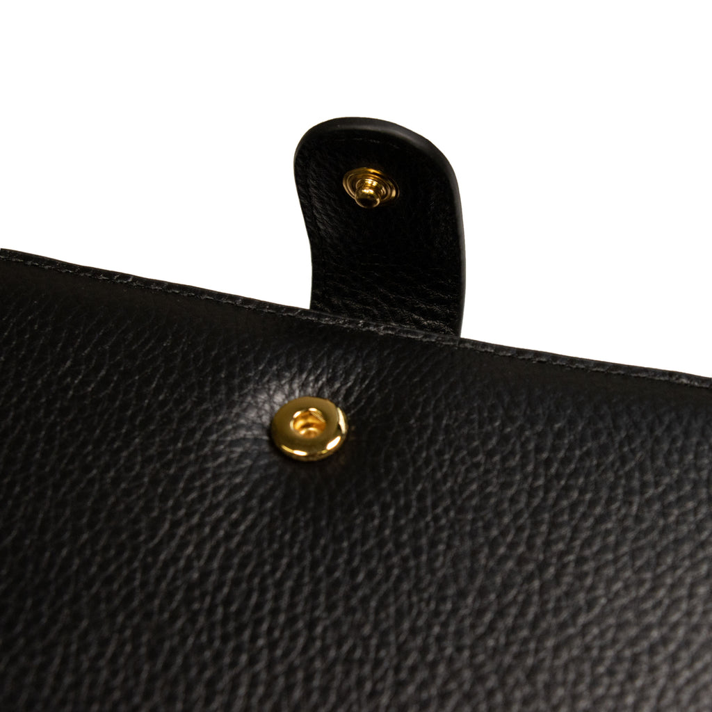 Close up on the snap detail of a smooth black leather agenda cover with gold snap hardware.