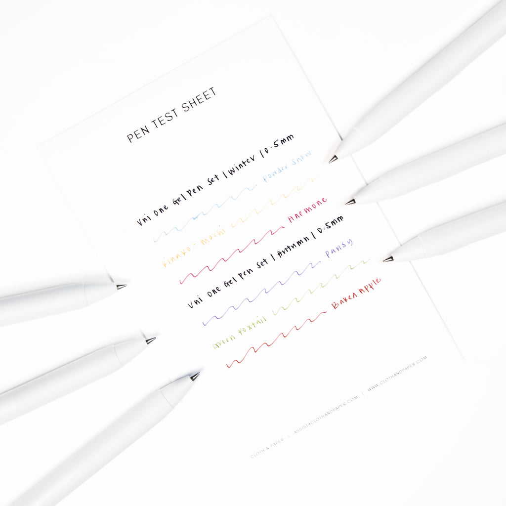 All six pen Uni One Limited Edition pens resting on a pent test sheet displaying a writing sample of each of the six ink colors.