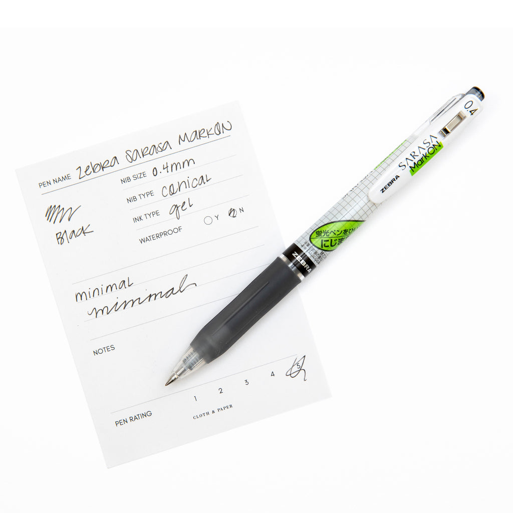 Pen in Black resting on a pen test sheet displaying a writing sample detailing the pen's specs.