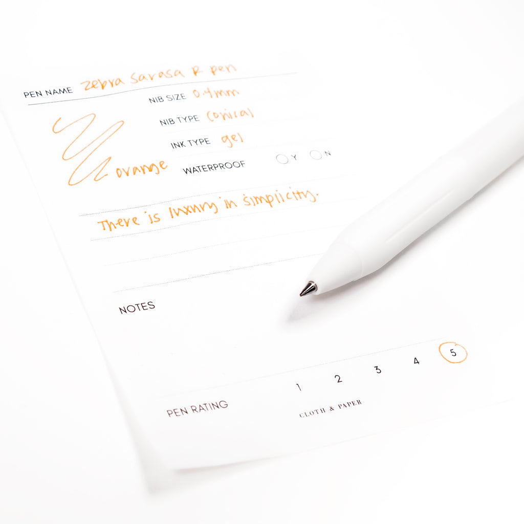 Zebra Sarasa R Pen, 0.4 mm, Orange, Cloth and Paper. Pen resting on pen test sheet displaying writing sample.
