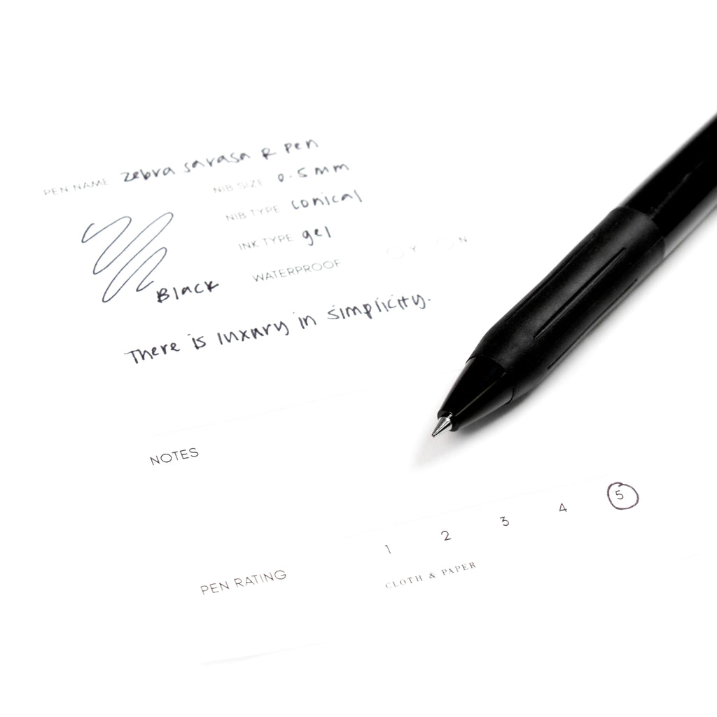 Zebra Sarasa R Pen, 0.5 mm, Black Ink, Black Body, Cloth and Paper. Close up on pen nib resting on pen test sheet.